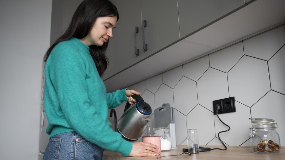 Chica prepara un café en la cocina con la cafetera enchufada a la corriente.