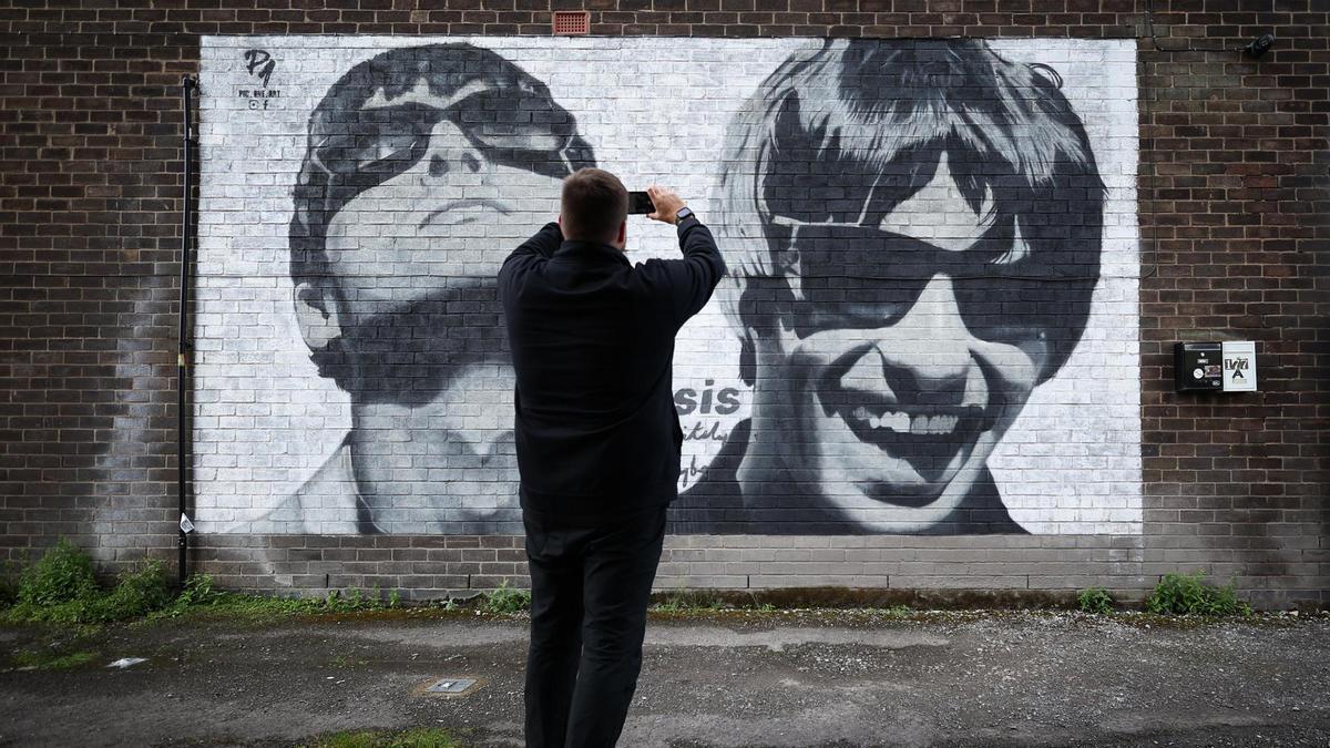 Un hombre fotografía un mural de la banda Oasis en Mánchester.