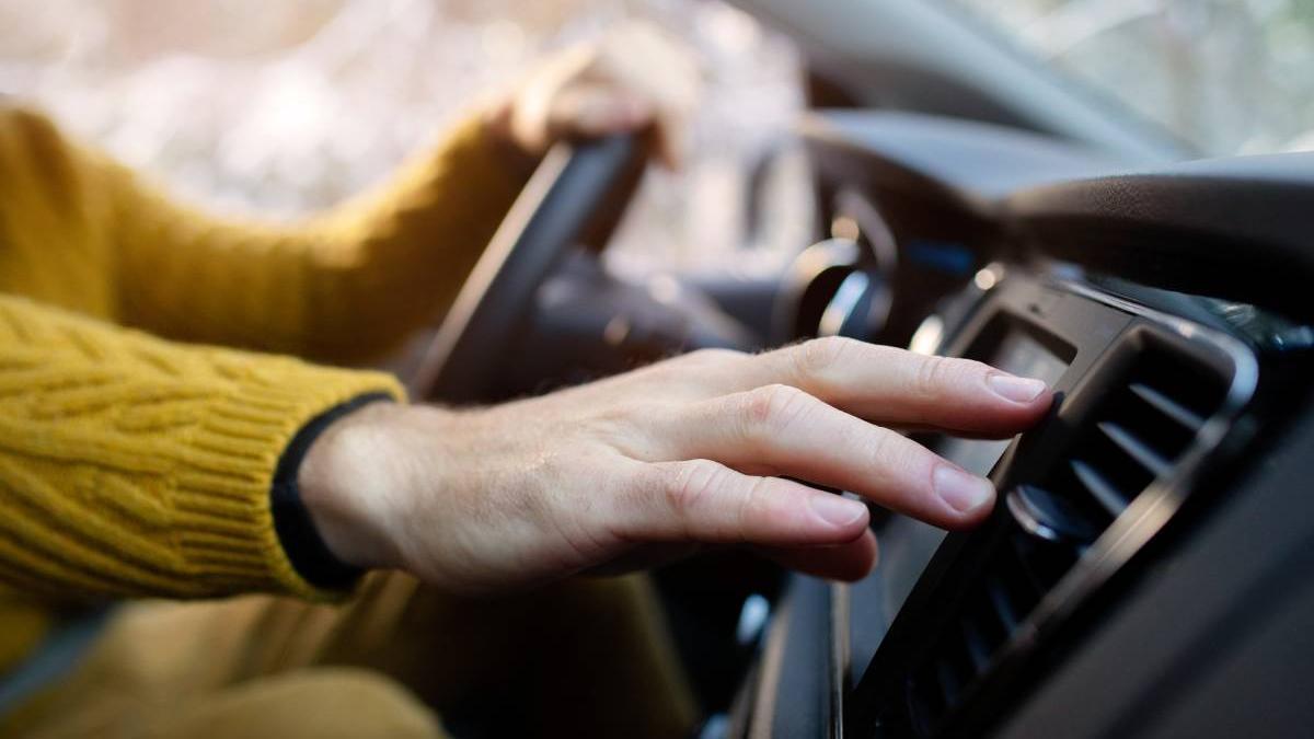 Mano de un hombre encendiendo la calefacción del coche mientras conduce