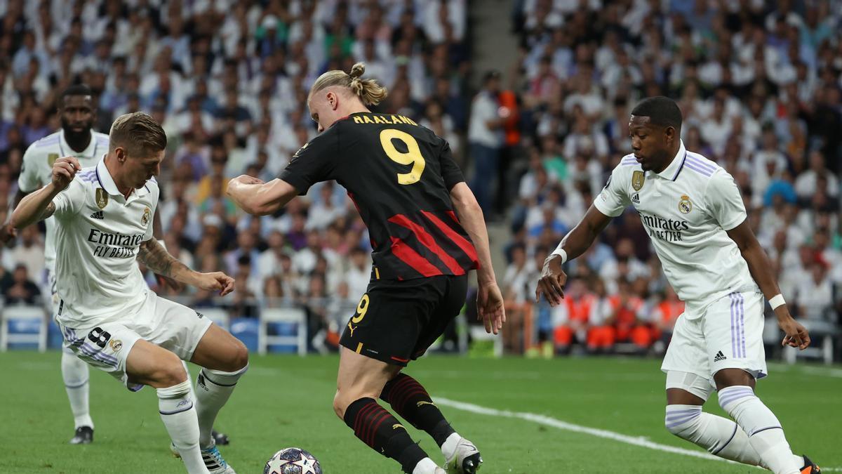 Erling Haaland (c) pelea un balón con Toni Kroos (i) y David Alaba.