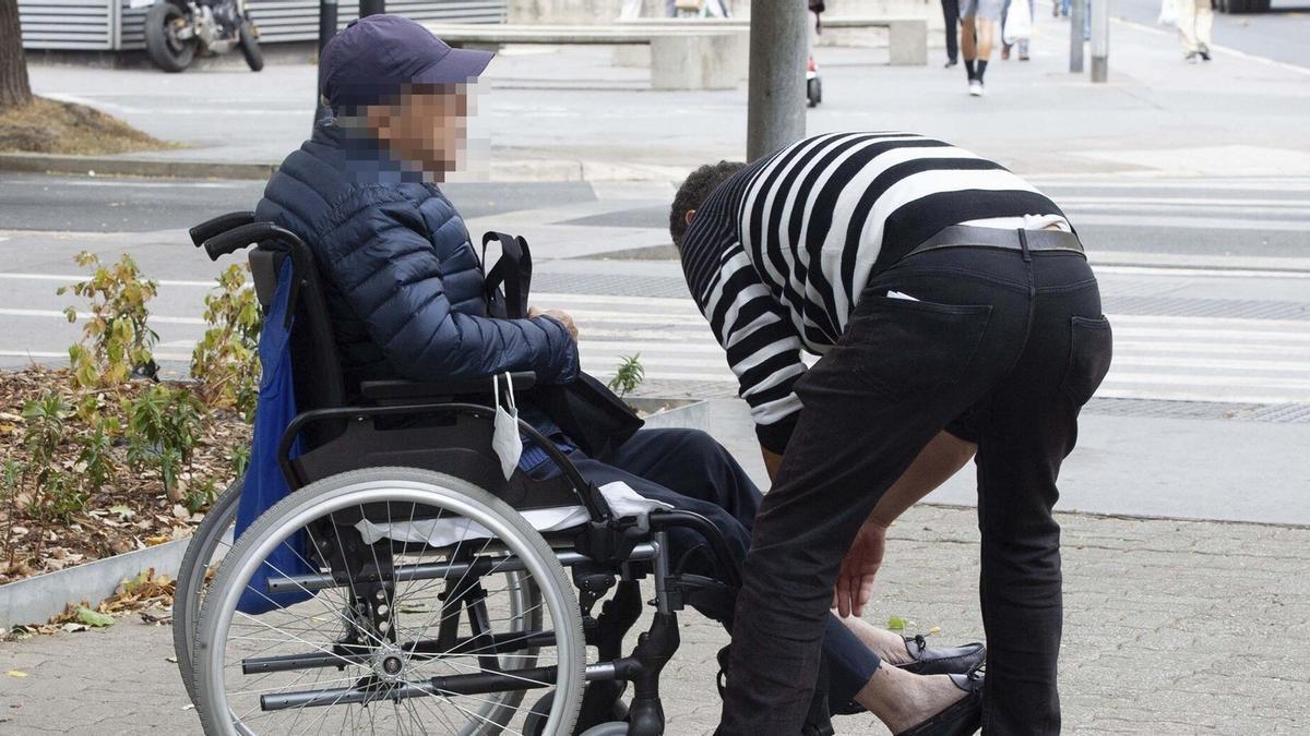 Una persona cuidadora atiende a un mayor en silla de ruedas.