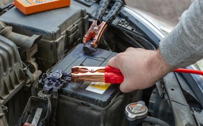 Una persona coloca pinzas en la batería del coche.
