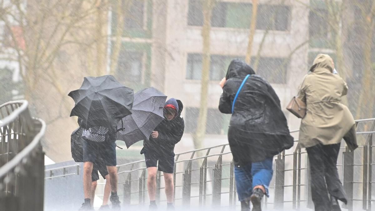 Varias personas tratan de hacer frente al viento y a la lluvia en Bilbao.