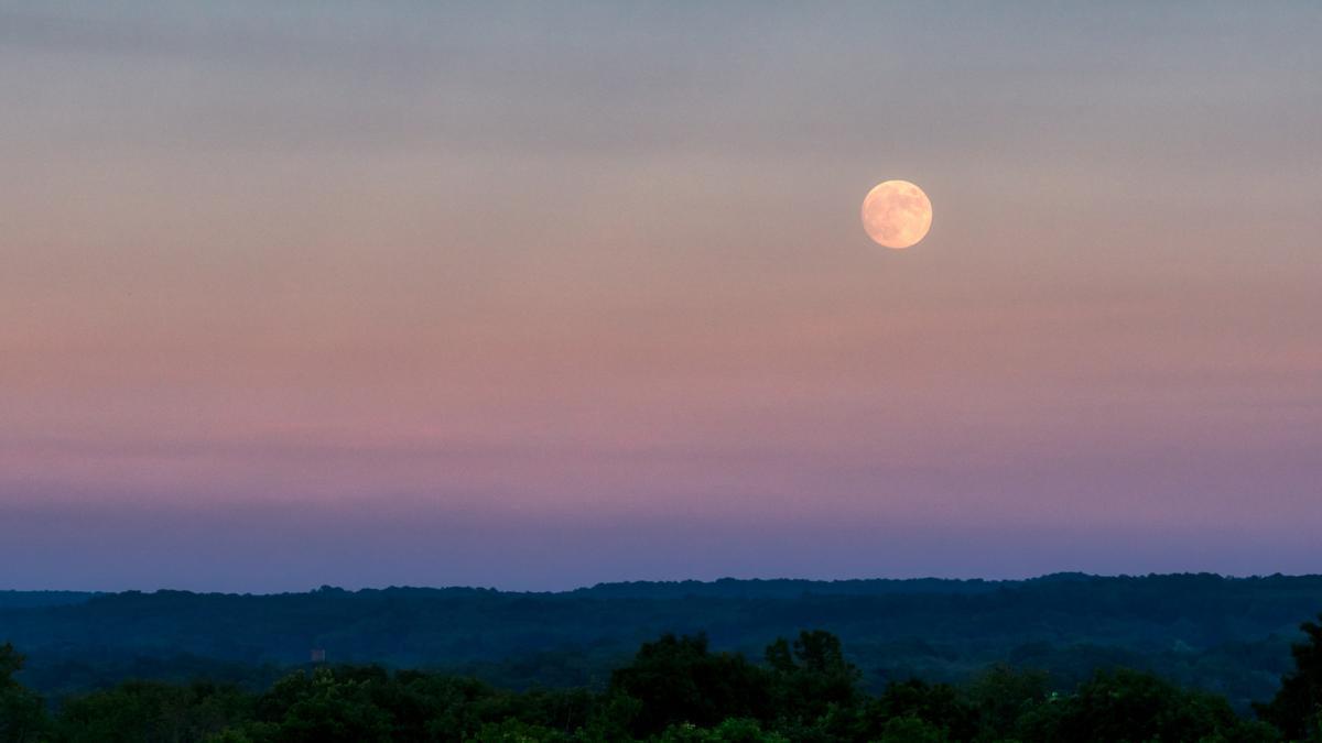 La luna llena se alza sobre un paisaje al amanecer.
