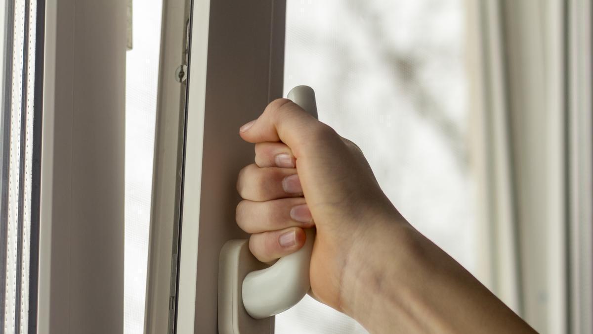 Primer plano de una mano abriendo la ventana para ventilar la casa.