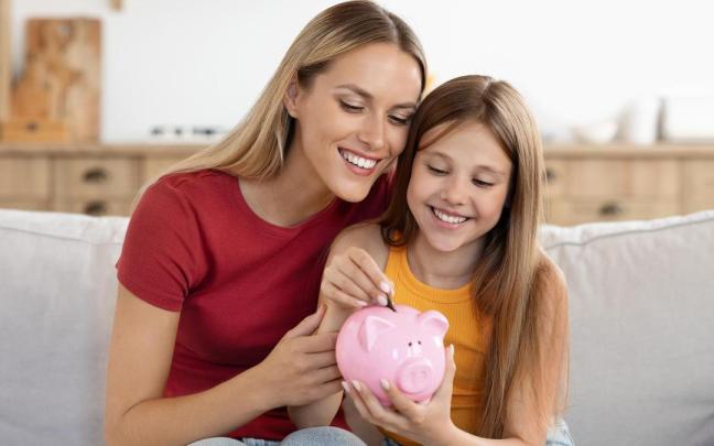 Una niña mete una moneda en una hucha.