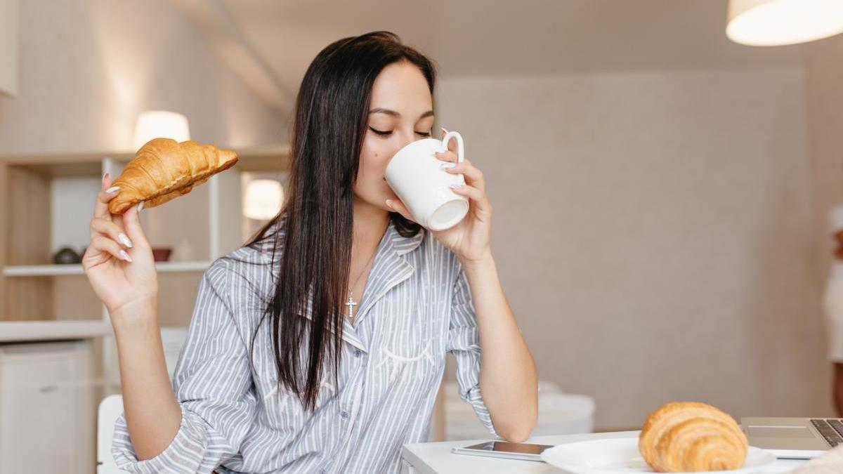 Chica desayuna café y un croissant.