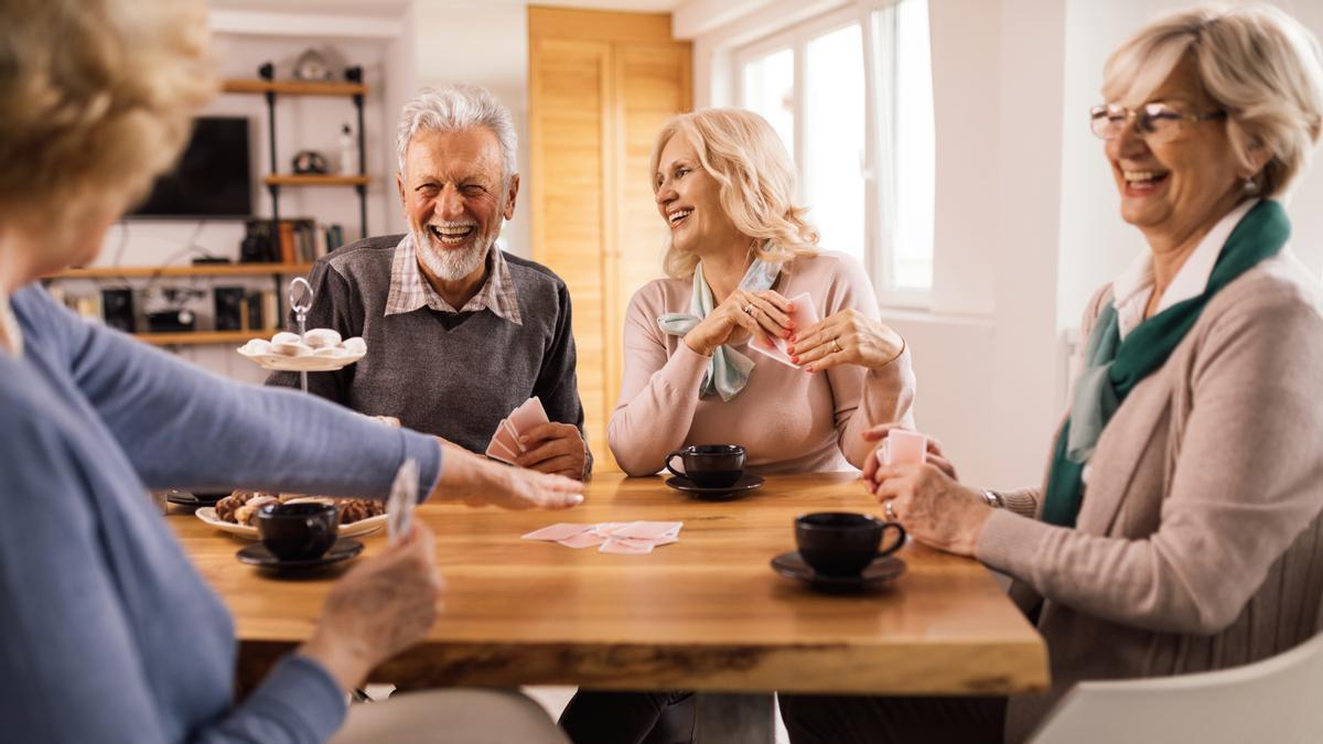 Personas mayores juegan a las cartas alrededor de una mesa.