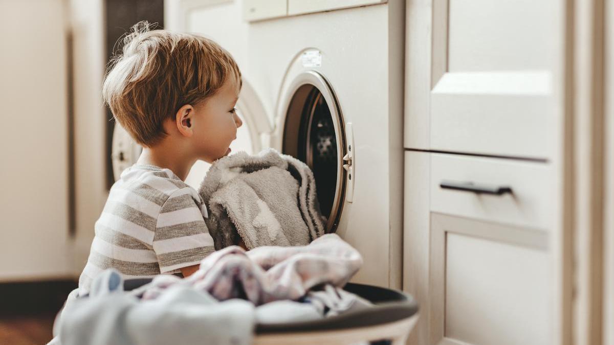 Un niño ayuda con las labores domésticas y mete algunas toallas a la lavadora.