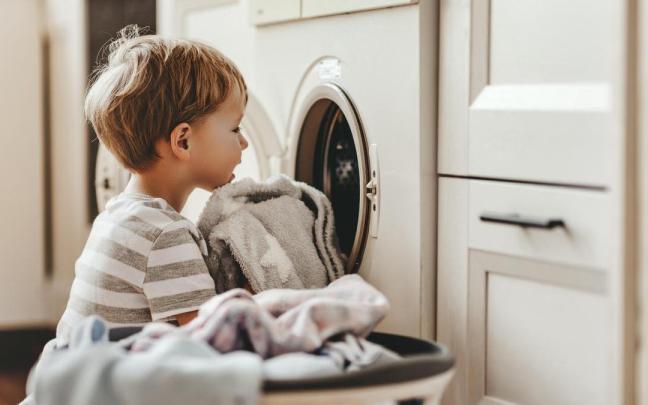 Un niño ayuda con las labores domésticas y mete algunas toallas a la lavadora. Un niño ayuda con las labores domésticas y mete algunas toallas a la lavadora.