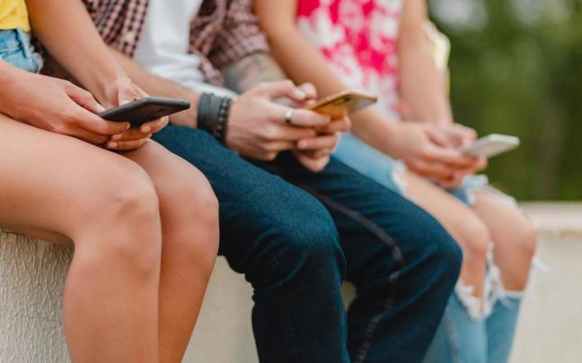 Tres menores con sus teléfonos móviles.