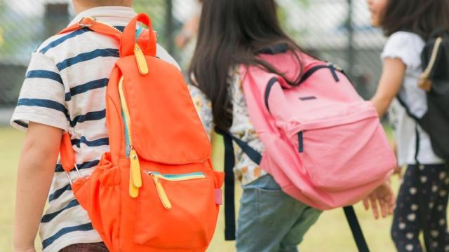 Tres niños van al colegio con sus mochilas.