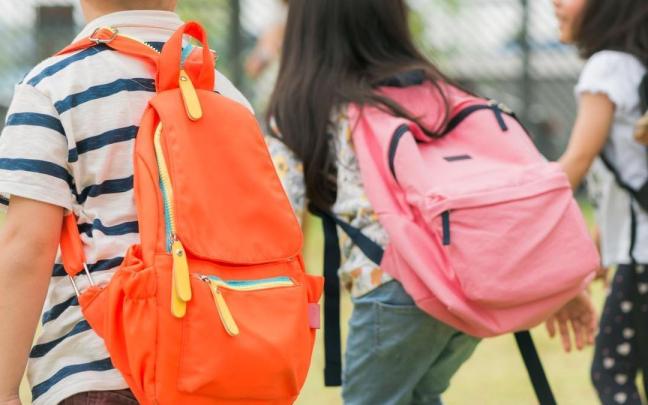 Tres niños van al colegio con sus mochilas.