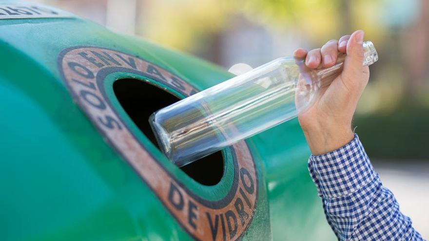 Un ciudadano deposita una botella en un contenedor verde.