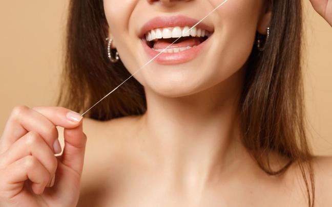 Una mujer se pasa el hilo dental por los dientes.