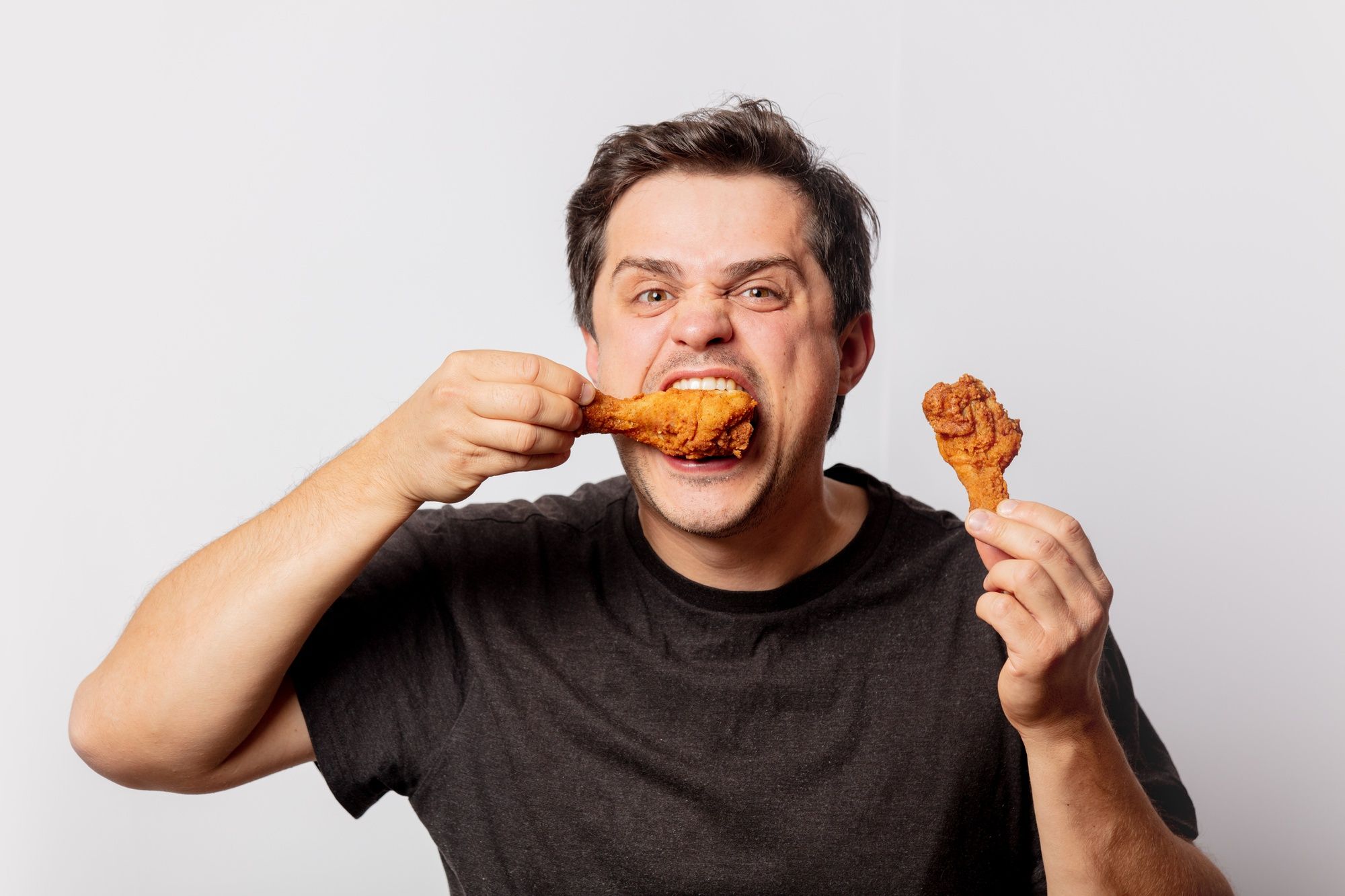 Un hombre devora dos muslitos de pollo.