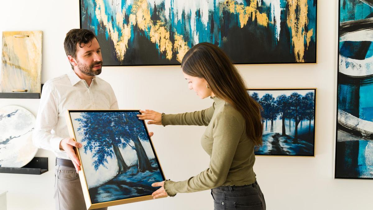 Un artista muestra una de sus pinturas a una clienta en una galería de arte.