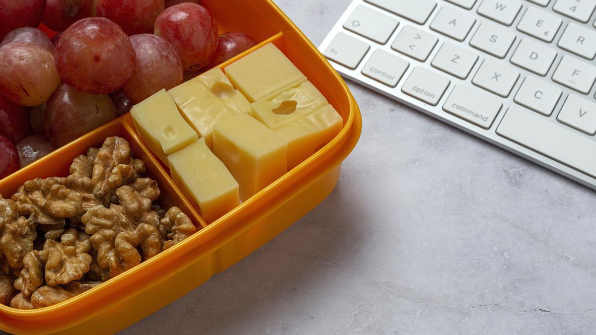 Un tupper con uvas, nueces y queso junto al teclado de un portátil.