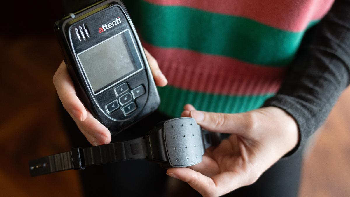 Una persona muestra una pulsera electrónica de geolocalización telemática y su monitor.