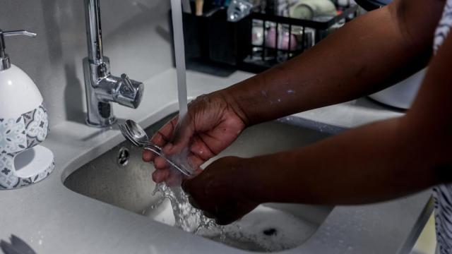 Una empleada de hogar friega cubiertos de cocina