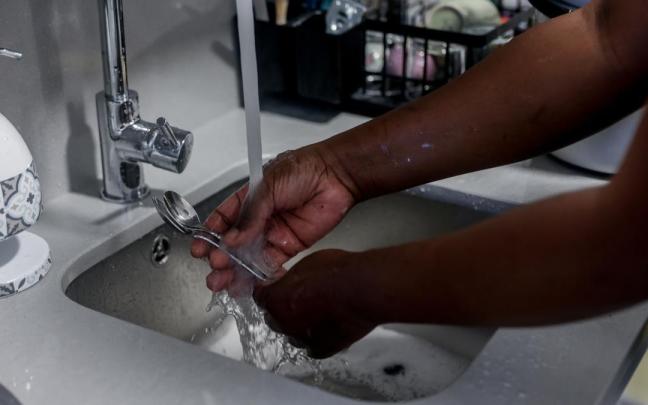 Una empleada de hogar friega cubiertos de cocina