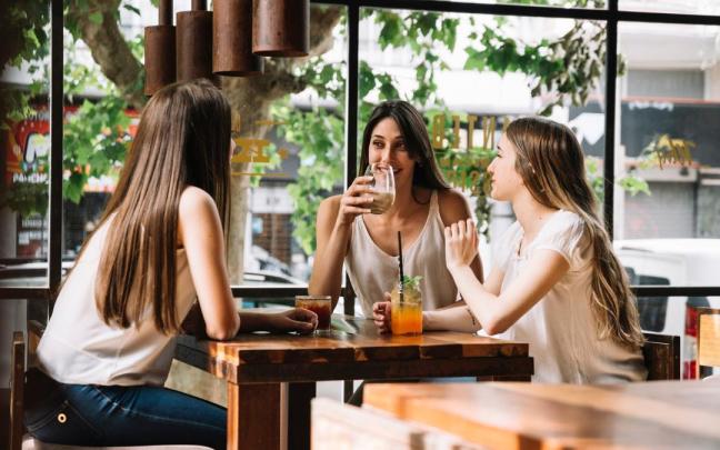 Tres amigas charlan distendidamente en una cafetería.