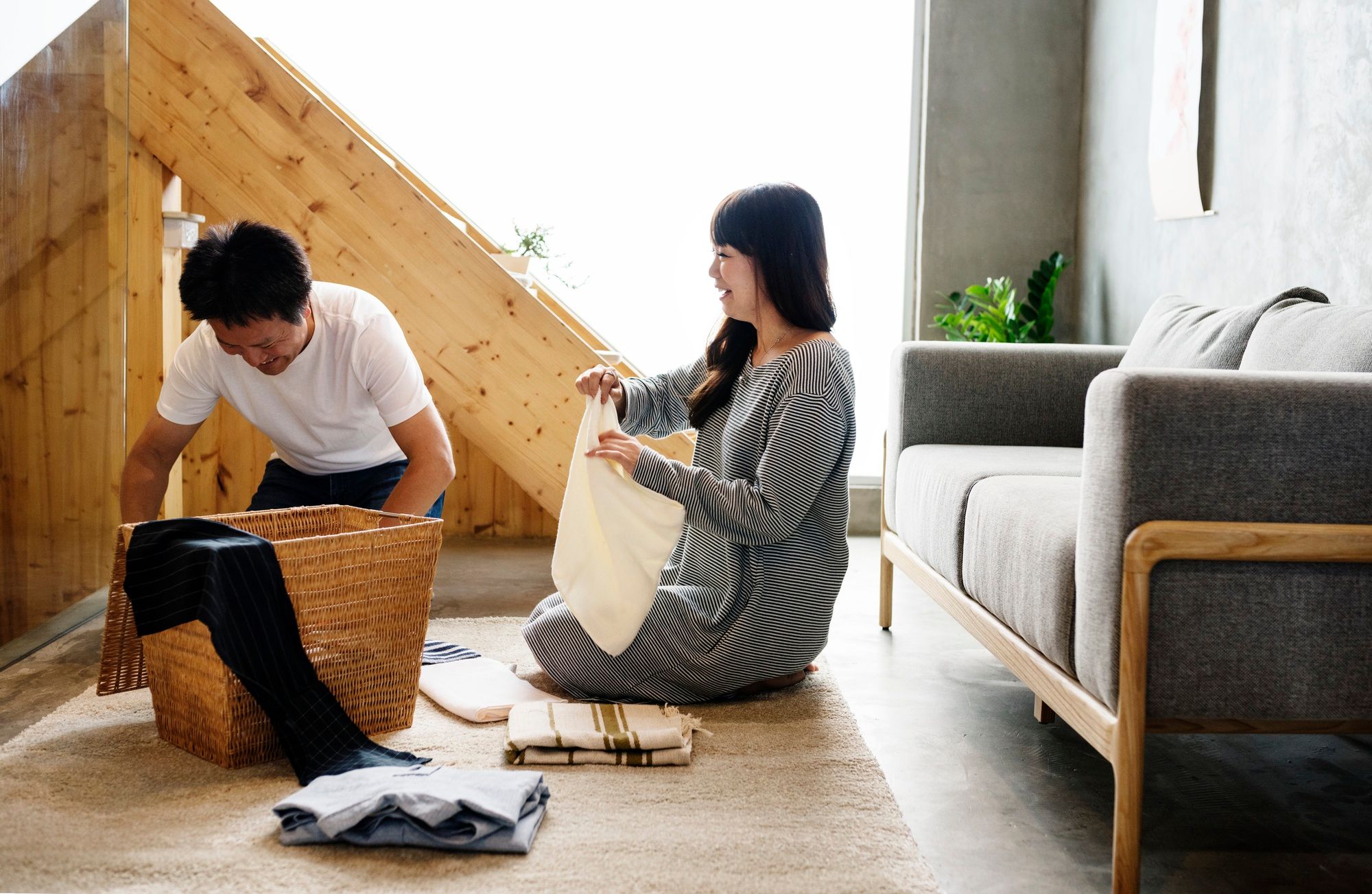 Una pareja, sentada en el suelo, recoge la ropa a un cesto.