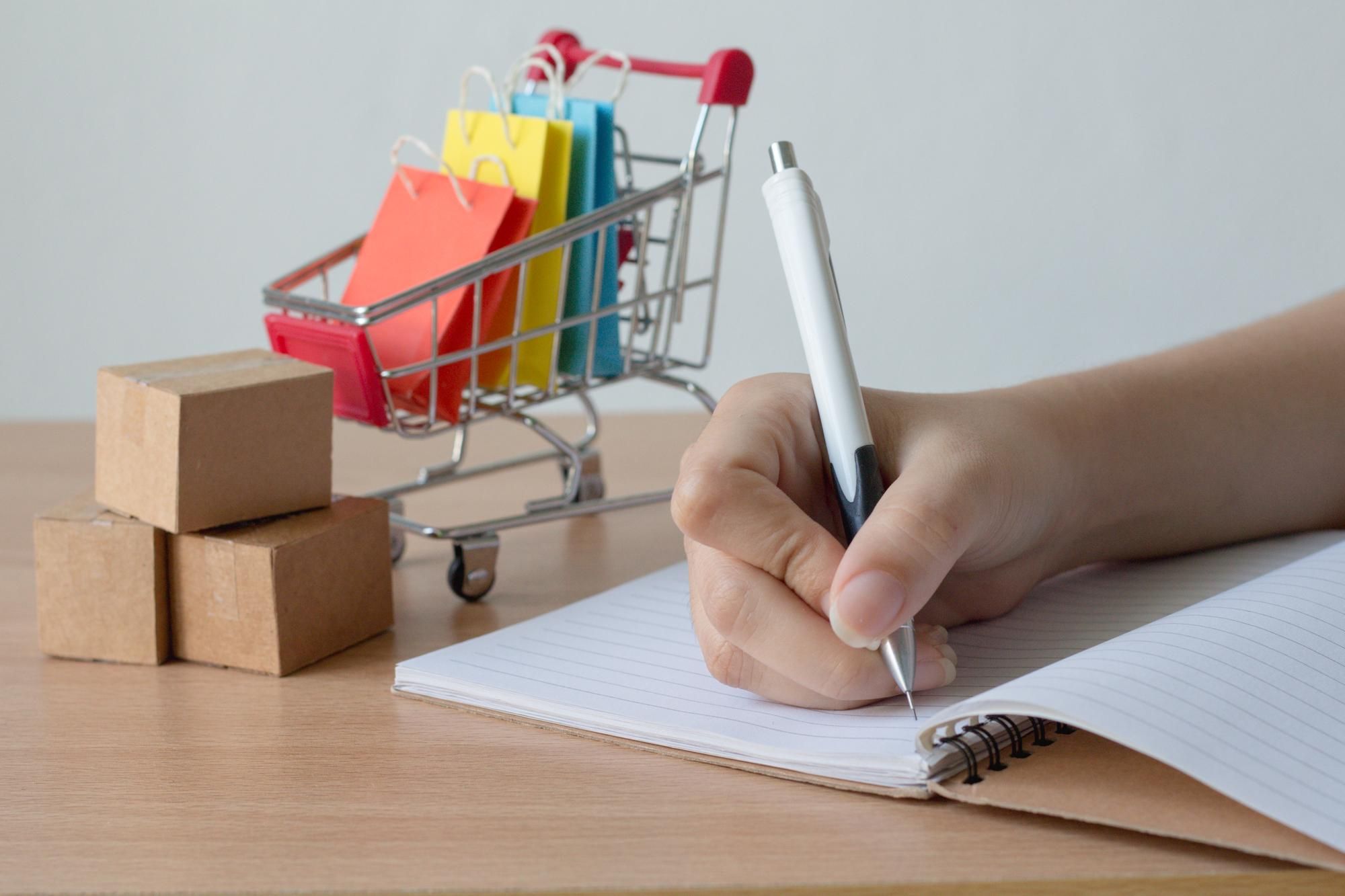 Una mujer elabora una lista de regalos junto a un pequeño carrito de compra.
