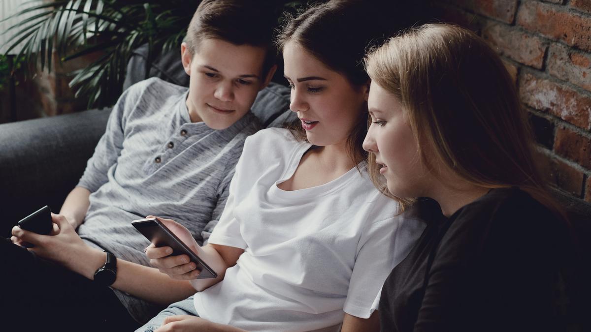 Tres adolescentes miran atentos a un móvil.