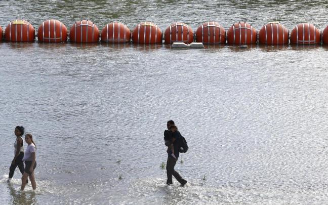 Varios migrantes pasan junto a la barrera de boyas alambradas.