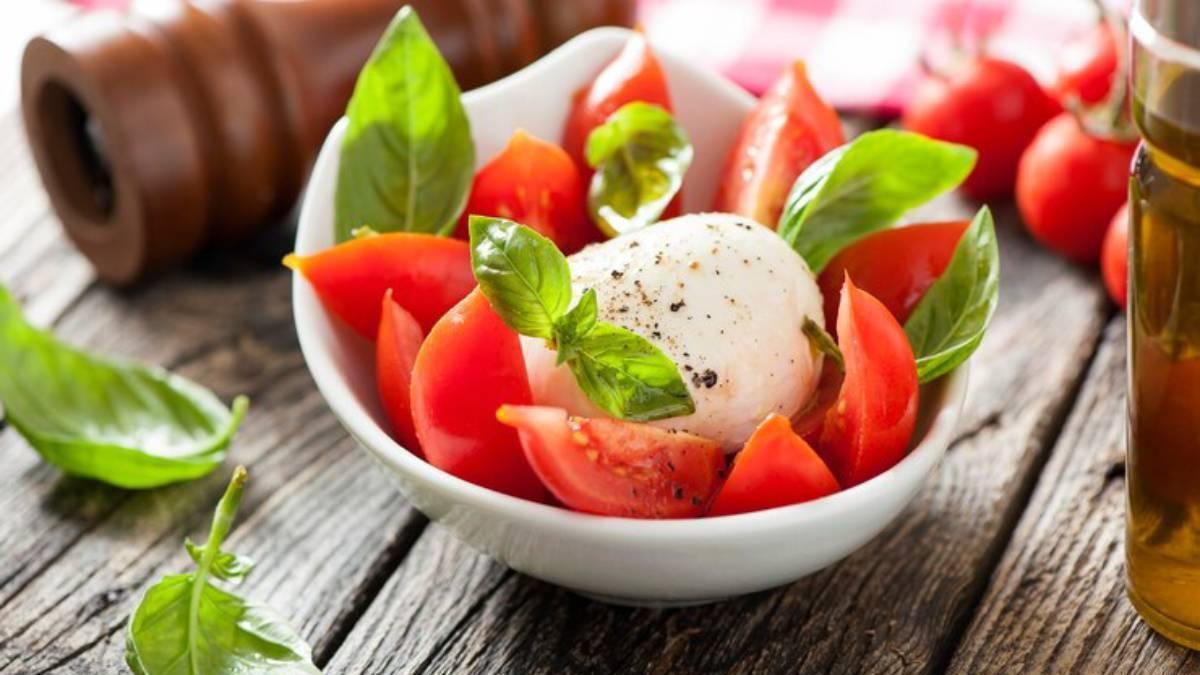 Ensalada de tomate con burrata sobre una mesa de madera.