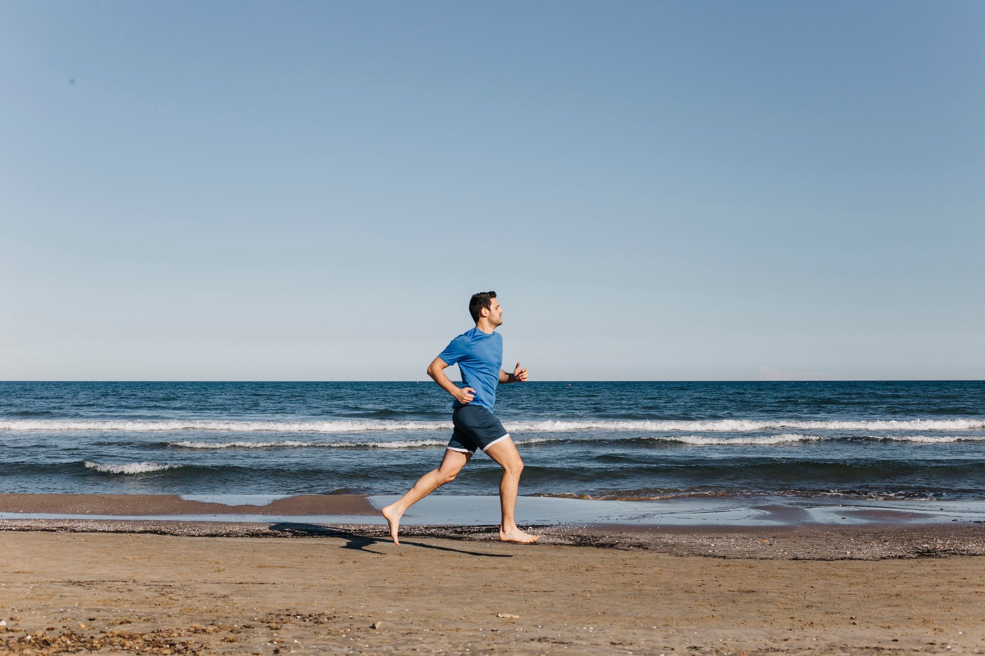 Un hombre corre descalzo por la playa.