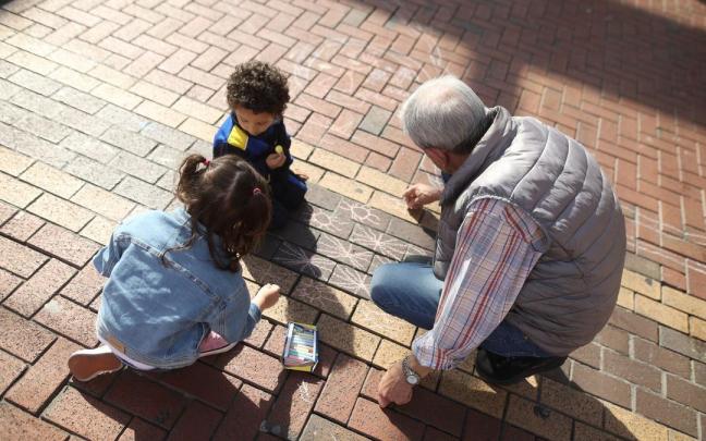 Un hombre mayor juega con unos niños, en la plaza San Pedro de Sestao.