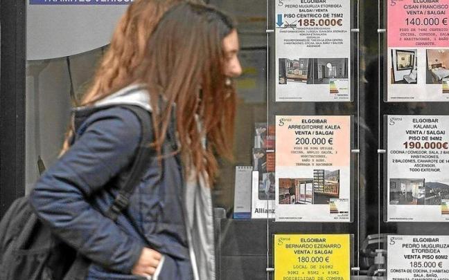 Dos jóvenes caminan frente al escaparate de una inmobiliaria que anuncia pisos a la venta en Elgoibar. Dos jóvenes caminan frente al escaparate de una inmobiliaria que anuncia pisos a la venta en Elgoibar.