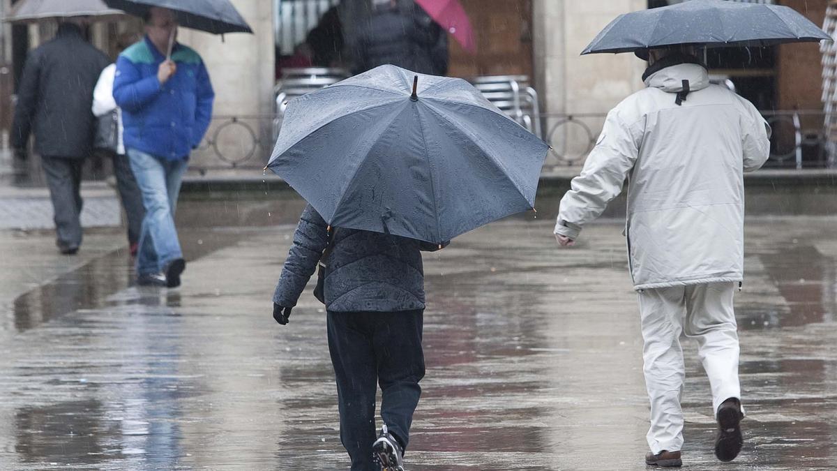 Varias personas se refugian de la lluvia bajo sus paraguas.