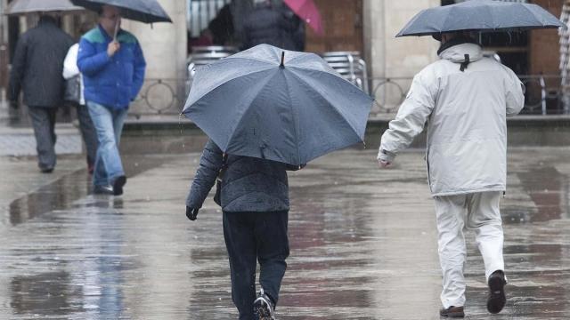 Varias personas se refugian de la lluvia bajo sus paraguas.