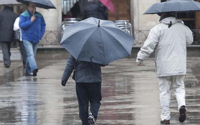 Varias personas se refugian de la lluvia bajo sus paraguas.