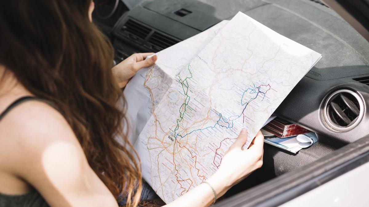 Joven consulta un mapa físico en el coche.