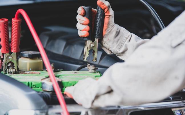 Un mecánico intenta arrancar un coche conectando unas pinzas a la batería.