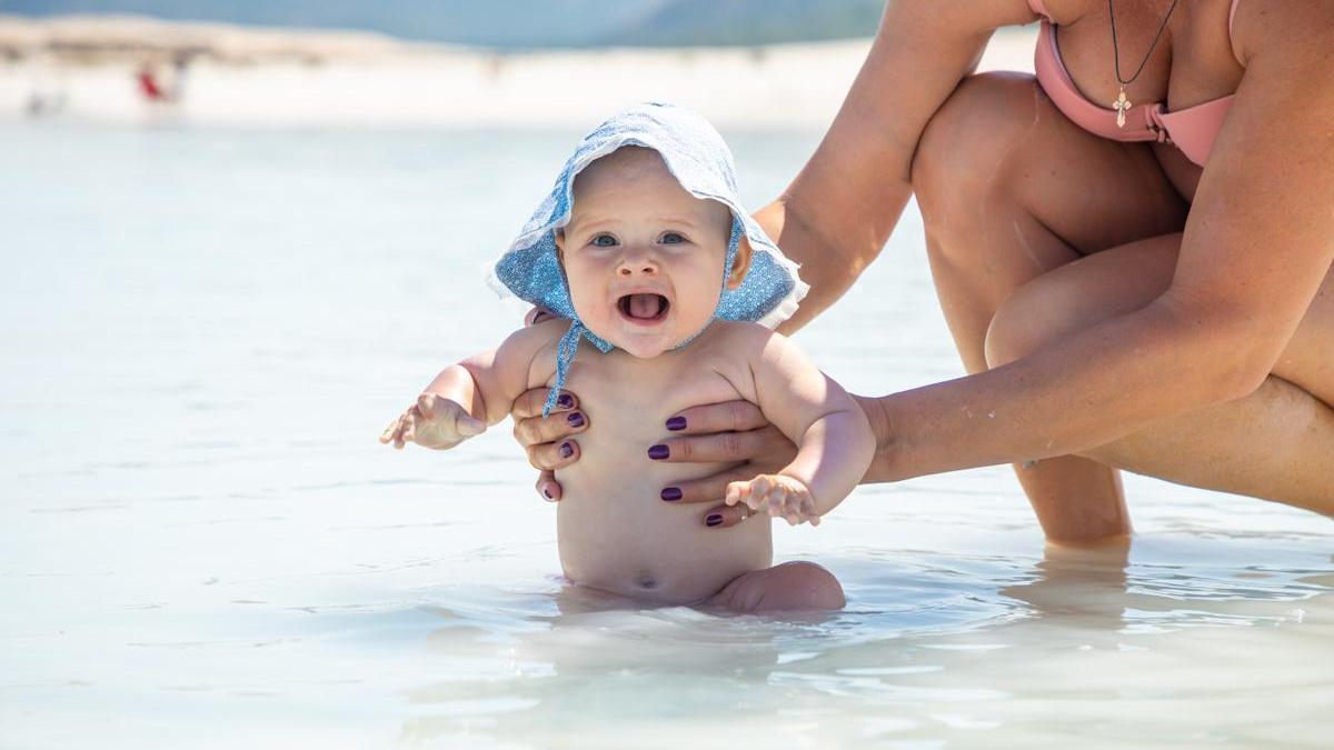 Bebé se baña en la orilla con su madre.