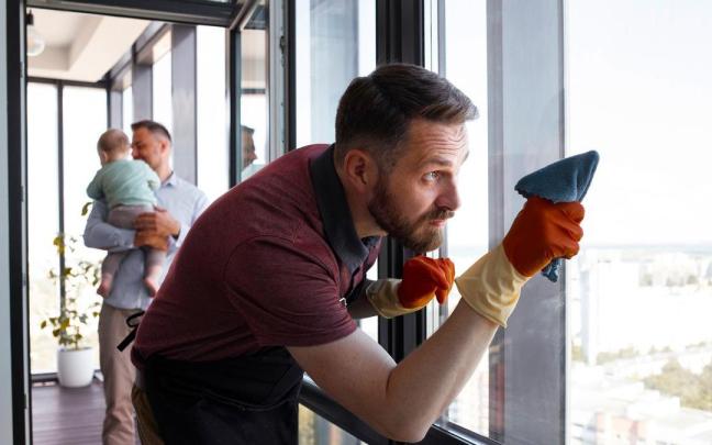 Un hombre limpia con esmero el cristal de una ventana.