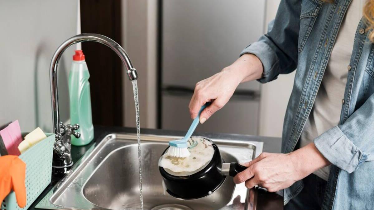 Chica limpia una olla con ayuda de un cepillo para eliminar toda la grasa incrustada.