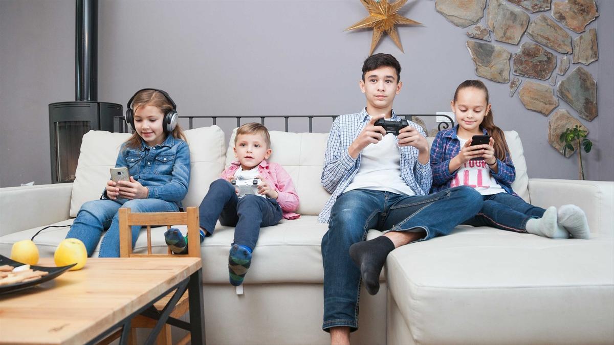 Niños sentados en el sofá con diferentes pantallas.