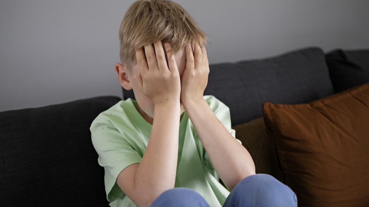 Un niño se tapa la cara con sus manos en señal de tristeza.