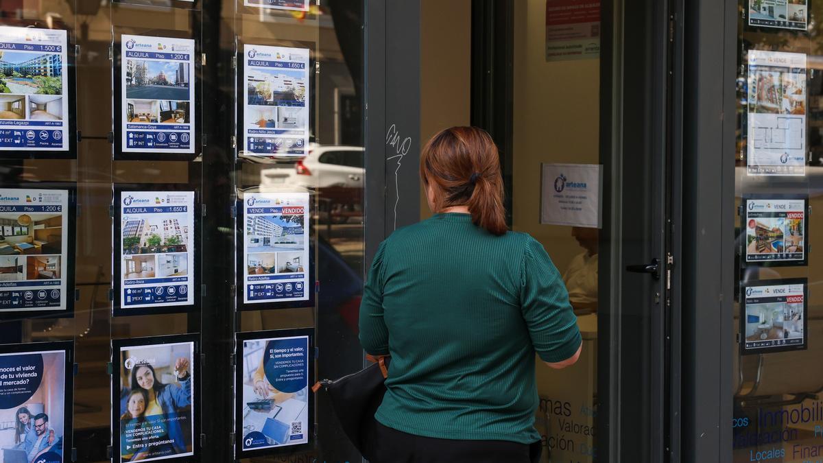 Una mujer contempla la oferta de pisos en el escaparate de una inmobiliaria.