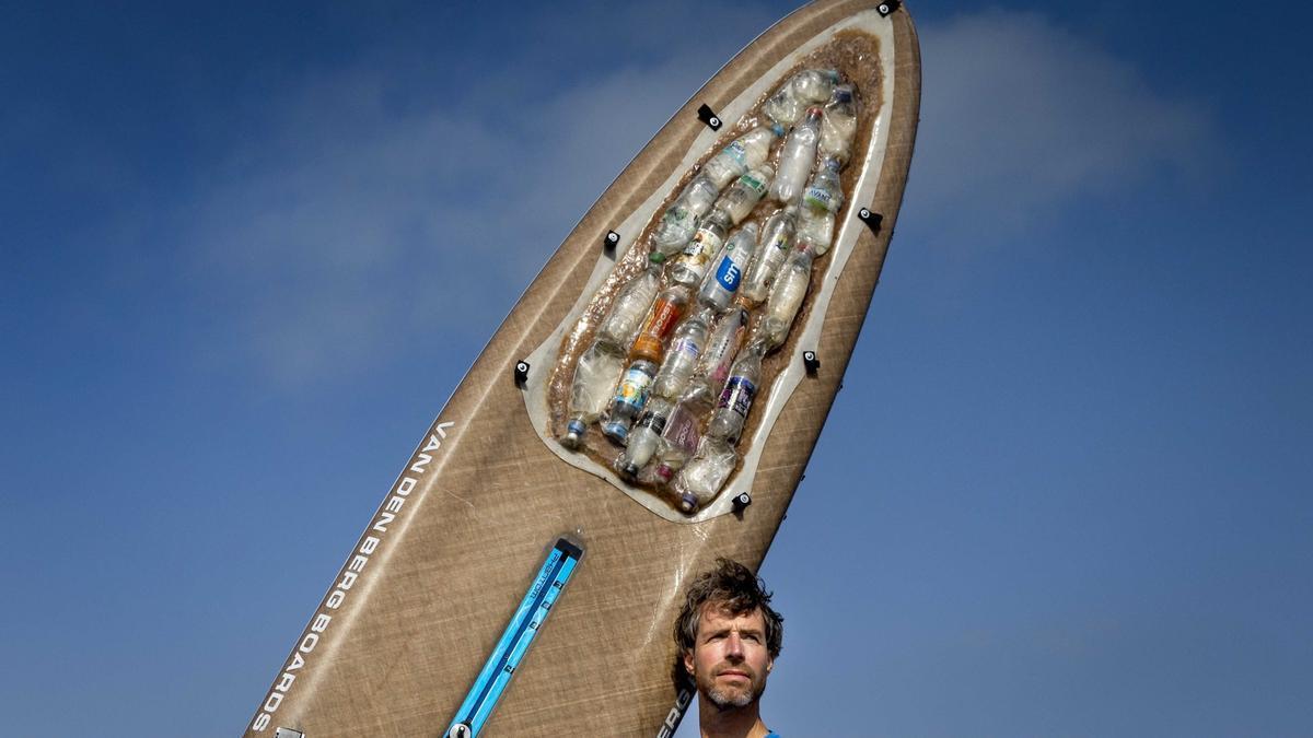 Un activista enseña su tabla de surf con restos de plásticos recogidos del mar.