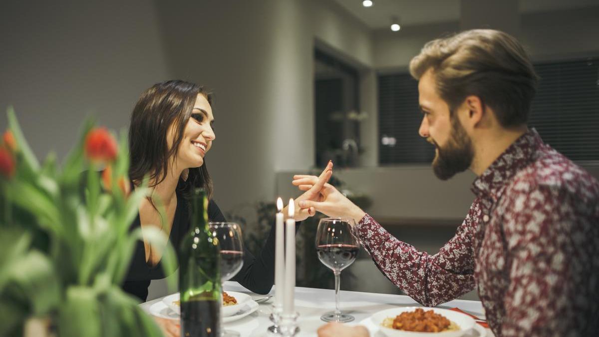 Pareja disfruta de una cena romántica en casa con velas y una botella de vino.