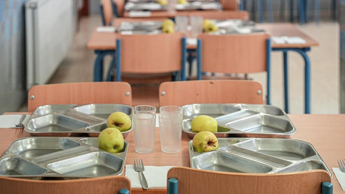 Varias mesas con bandejas de comida en un comedor escolar.