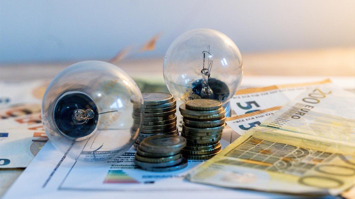 Dos bombillas sobre una factura junto a billetes y monedas de euro.
