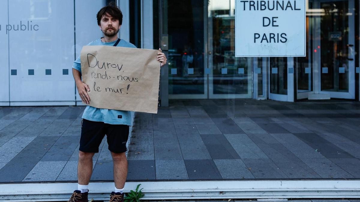 Un hombre posa frente al Tribunal Judicial de París con un cartel que dice: “Durov, devuélvenos el muro”.